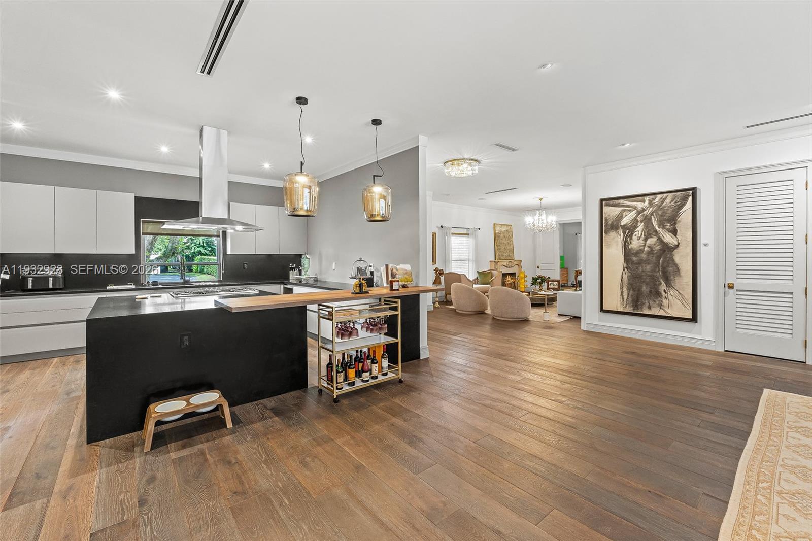 A modern kitchen with a black island and wood bar opens into a living area — 680 Buttonwood Ln, Miami FL 33137, MIAMI, FL