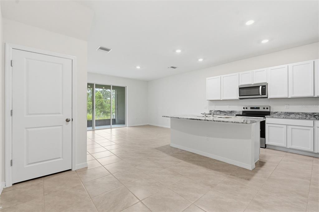 A kitchen with white cabinets and a granite island opens into a tiled living area — 5005 GILDED BARD COURT, WIMAUMA, FL