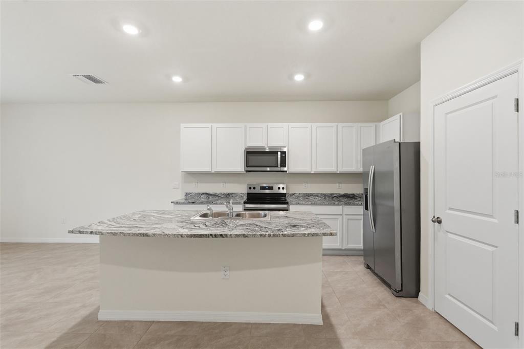 A kitchen features white cabinets, granite countertops, stainless steel appliances, and a central island — 5005 GILDED BARD COURT, WIMAUMA, FL