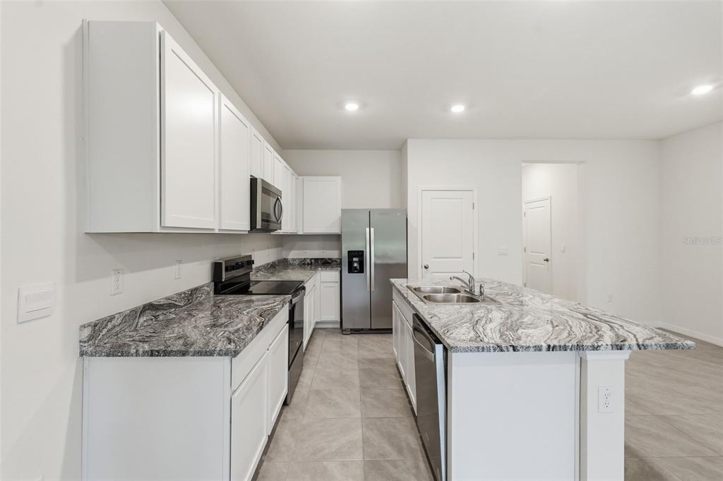 A modern kitchen features white cabinets, granite countertops, stainless steel appliances, and a center island — 5005 GILDED BARD COURT, WIMAUMA, FL