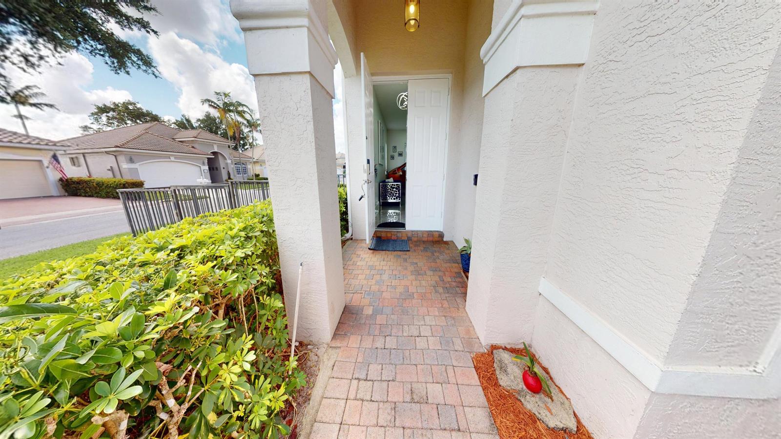A brick walkway leads to an open front door of a house with stucco walls — 8586 White Cay, West Palm Beach FL 33411, WEST PALM BEACH, FL
