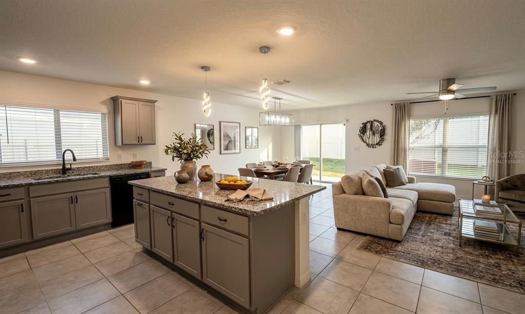 An open-concept kitchen with a granite island, gray cabinets, and an adjacent living area — 1842 GOLD CREST DRIVE, ST CLOUD, FL