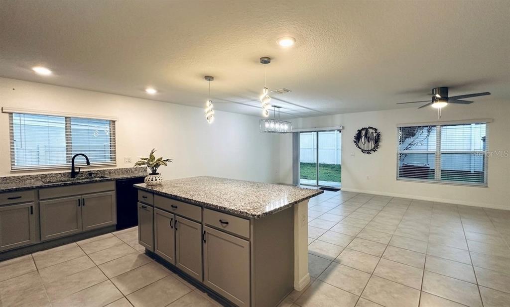 A kitchen with a granite-topped island and gray cabinets opens into a tiled living area — 1842 GOLD CREST DRIVE, ST CLOUD, FL