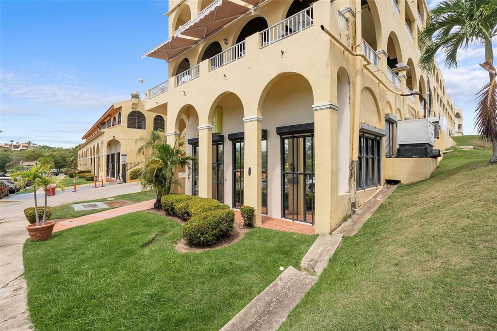 A multi-story yellow building with arched walkways and a grassy lawn in the foreground — 295 PALMAS INN WAY UNIT C11, HUMACAO, PR