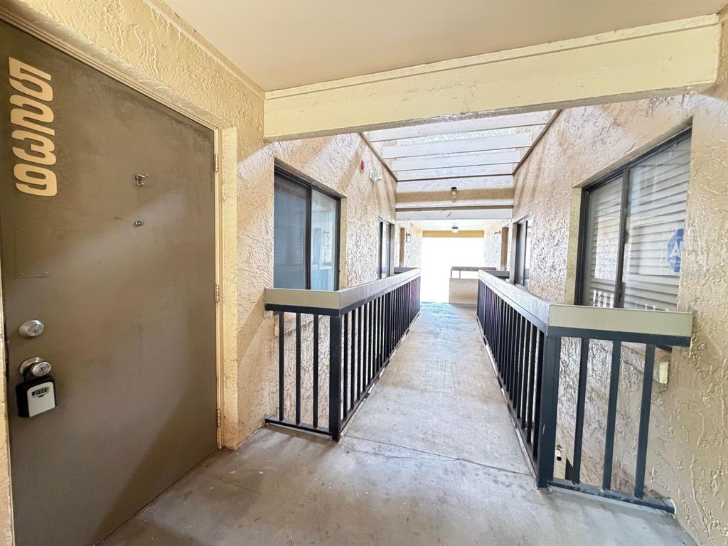 An exterior apartment hallway features a metal door, black railings, and a concrete walkway — 5239 VINELAND ROAD UNIT A203, ORLANDO, FL