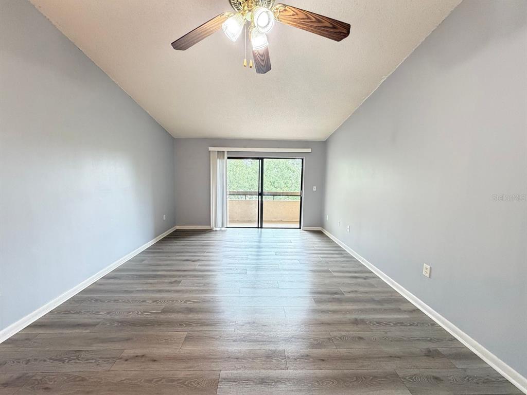 An empty room features light gray walls, wood-look flooring, a ceiling fan, and sliding glass doors — 5239 VINELAND ROAD UNIT A203, ORLANDO, FL