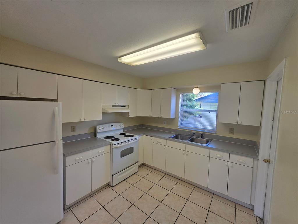 A kitchen with white cabinets, white appliances, gray countertops, and light-colored tile flooring — 7334 PONDEROSA DRIVE, TAMPA, FL