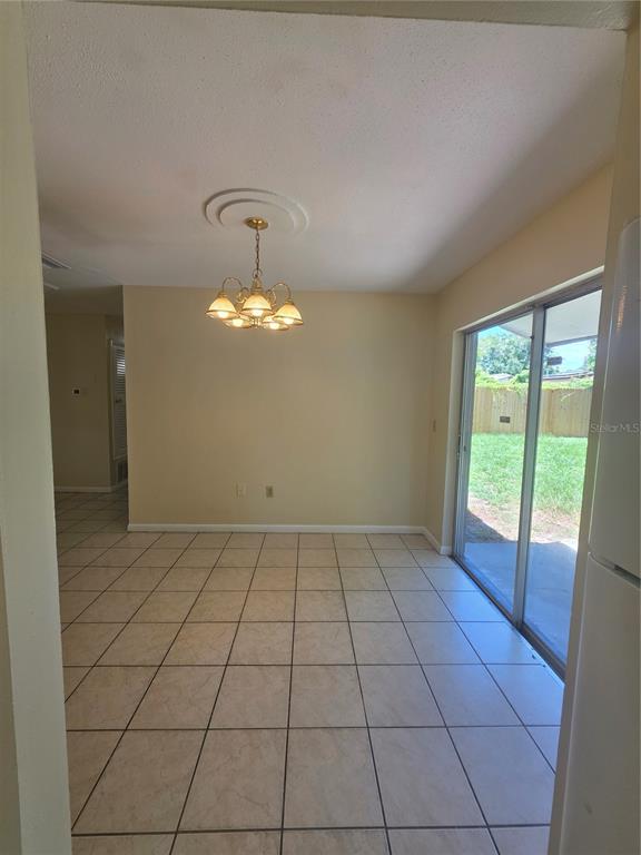 A dining area with beige walls, tile flooring, a chandelier, and a sliding glass door — 7334 PONDEROSA DRIVE, TAMPA, FL