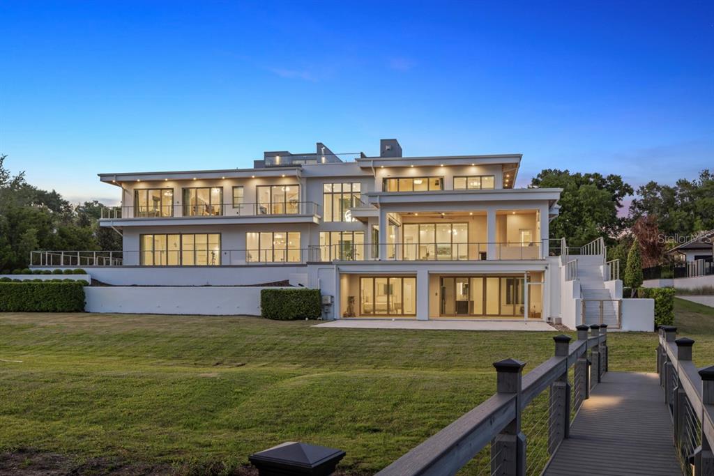 A large, modern multi-story house with white exterior walls and glass balconies overlooks a lawn — 9312 BLANCHE COVE DR, WINDERMERE, FL