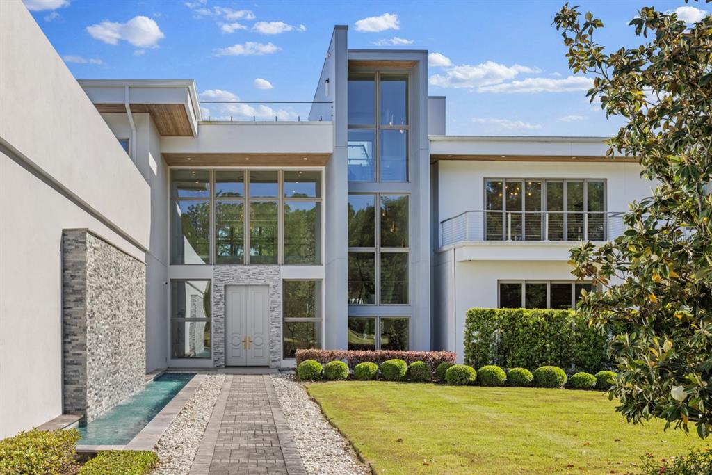 A modern two-story house features a stone water feature, glass facade, and a paved walkway — 9312 BLANCHE COVE DR, WINDERMERE, FL