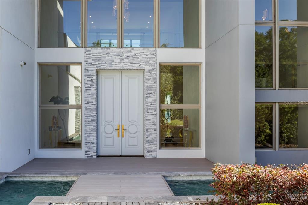 A modern home entrance features double doors, stone accents, and a bridge over water — 9312 BLANCHE COVE DR, WINDERMERE, FL