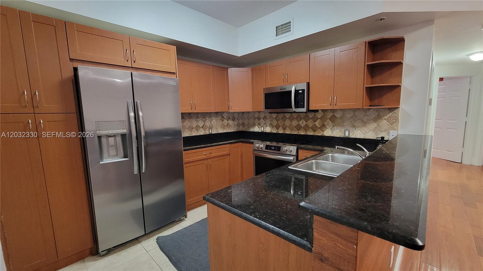 A kitchen features wood cabinets, black granite countertops, stainless steel appliances, and a tiled backsplash — 8430 SW 8th St # 307B, Miami FL 33144, MIAMI, FL