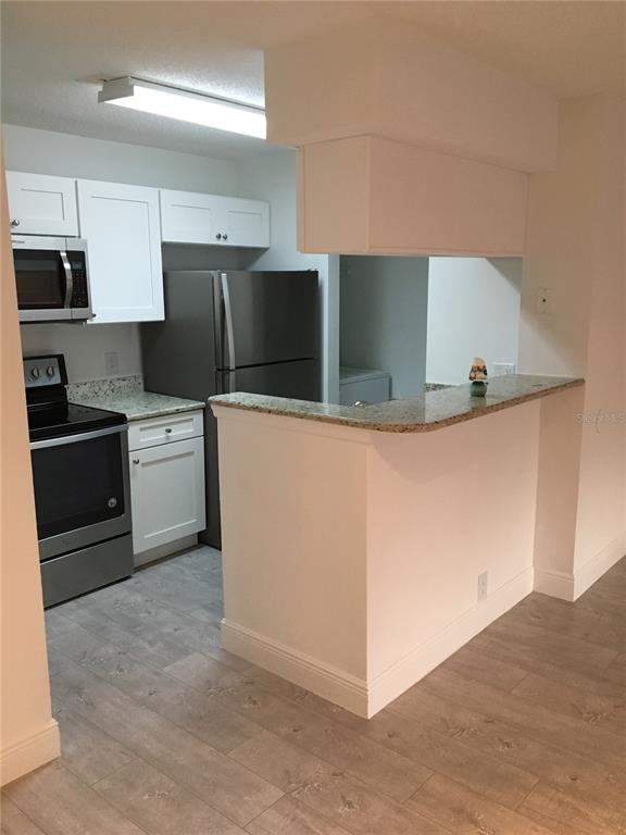 A kitchen features white cabinets, stainless steel appliances, and a granite-topped breakfast bar — 375 LAKE ONTARIO COURT UNIT 301, ALTAMONTE SPRINGS, FL