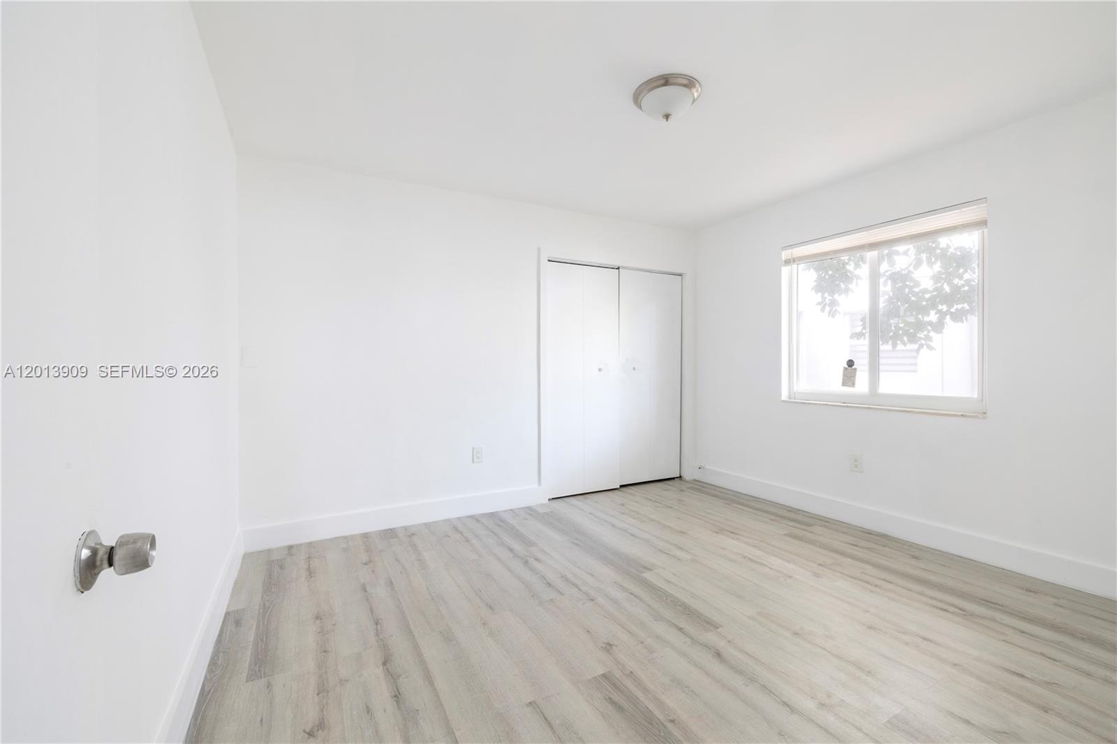 A bright, empty bedroom features white walls, light wood-look flooring, a closet, and a window — 1091 SW 4th St # 1, Miami FL 33130, MIAMI, FL