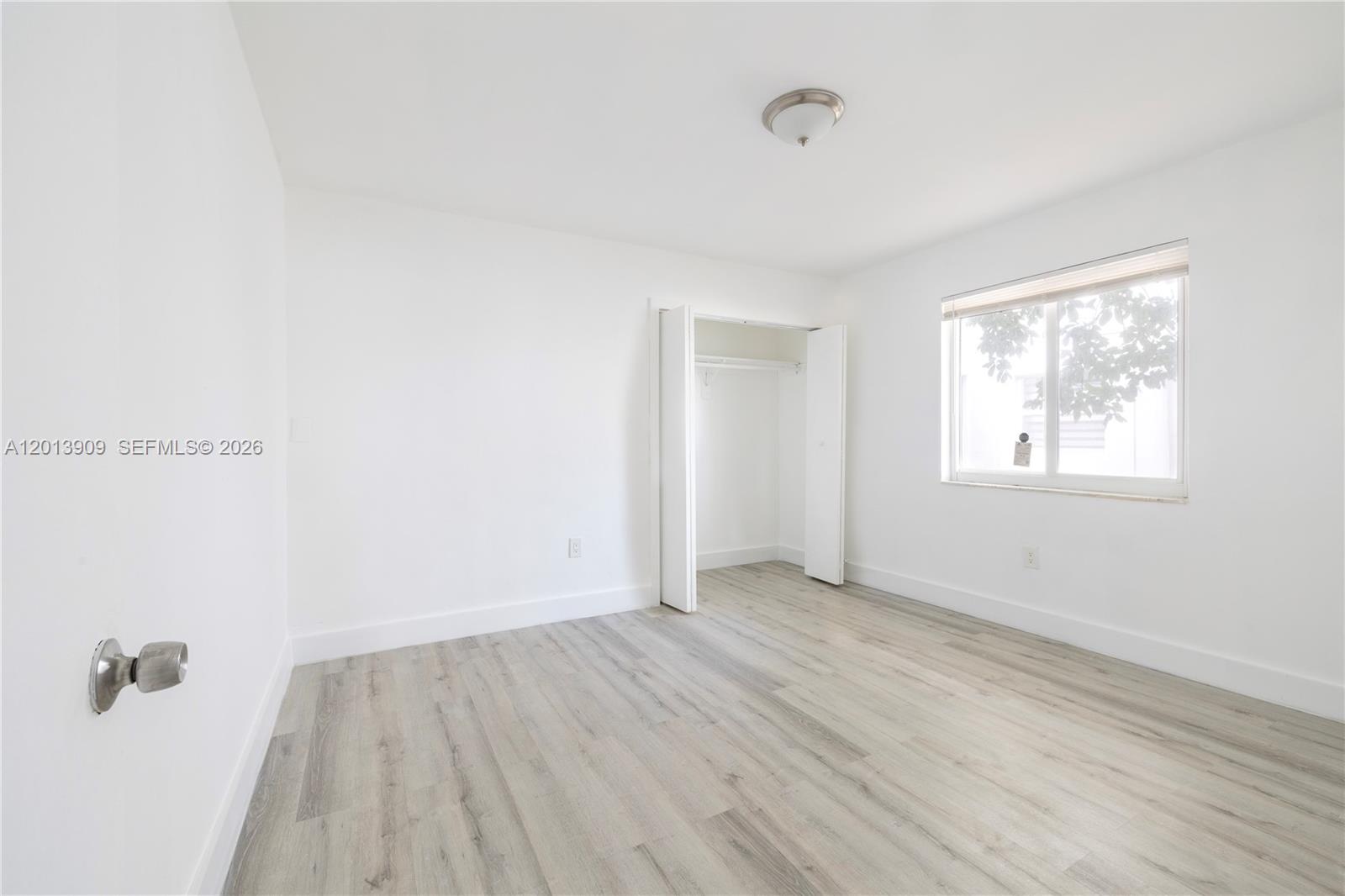 An empty bedroom features white walls, light wood-look flooring, a closet, and a window — 1091 SW 4th St # 1, Miami FL 33130, MIAMI, FL