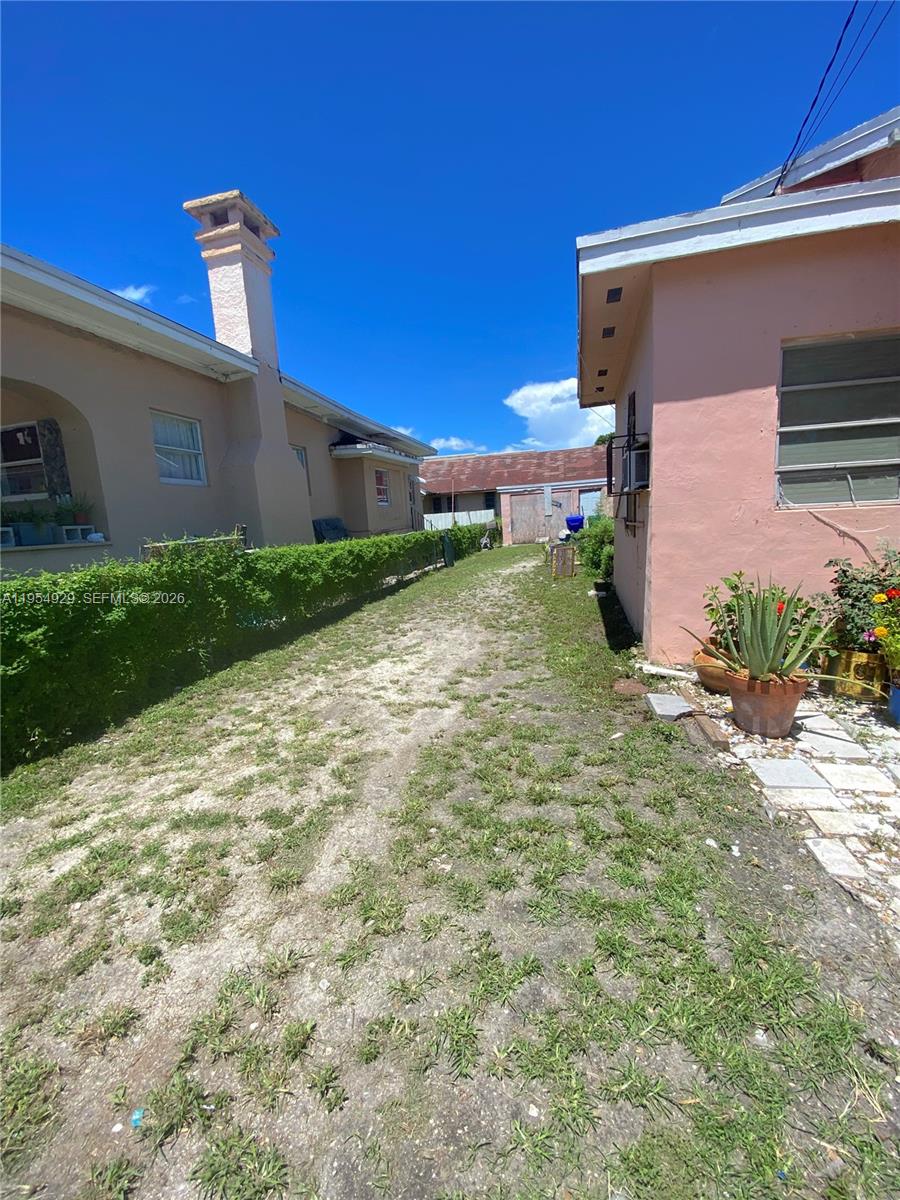 A narrow dirt path runs between two pink stucco houses under a clear blue sky — 114 NW 10th Ave, Miami FL 33128, MIAMI, FL