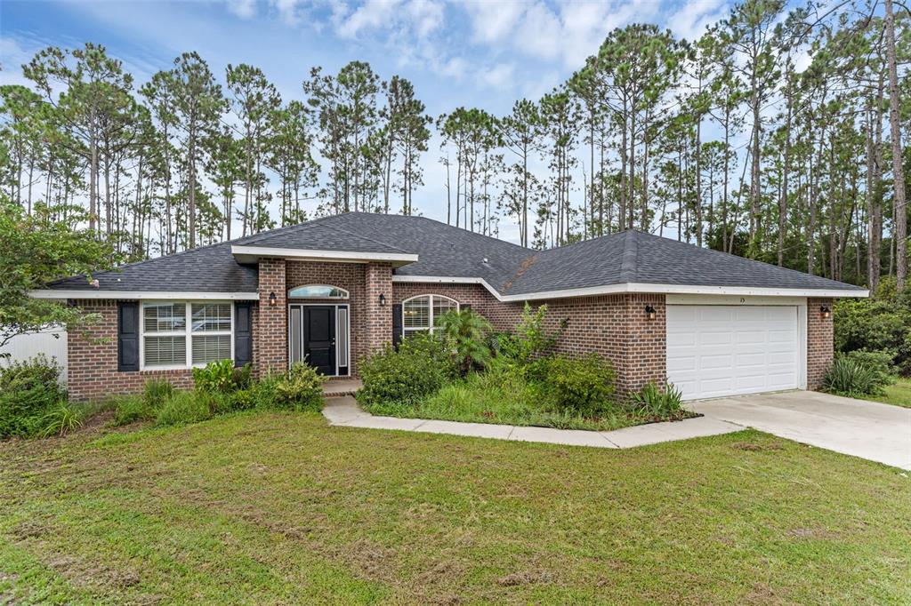 A single-story brick house with a two-car garage and a front walkway sits among trees — 15 ZELDA COURT, PALM COAST, FL
