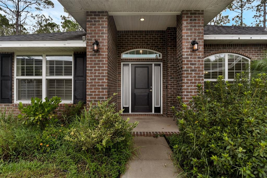 The front entrance of a brick house features a black door and a concrete walkway — 15 ZELDA COURT, PALM COAST, FL