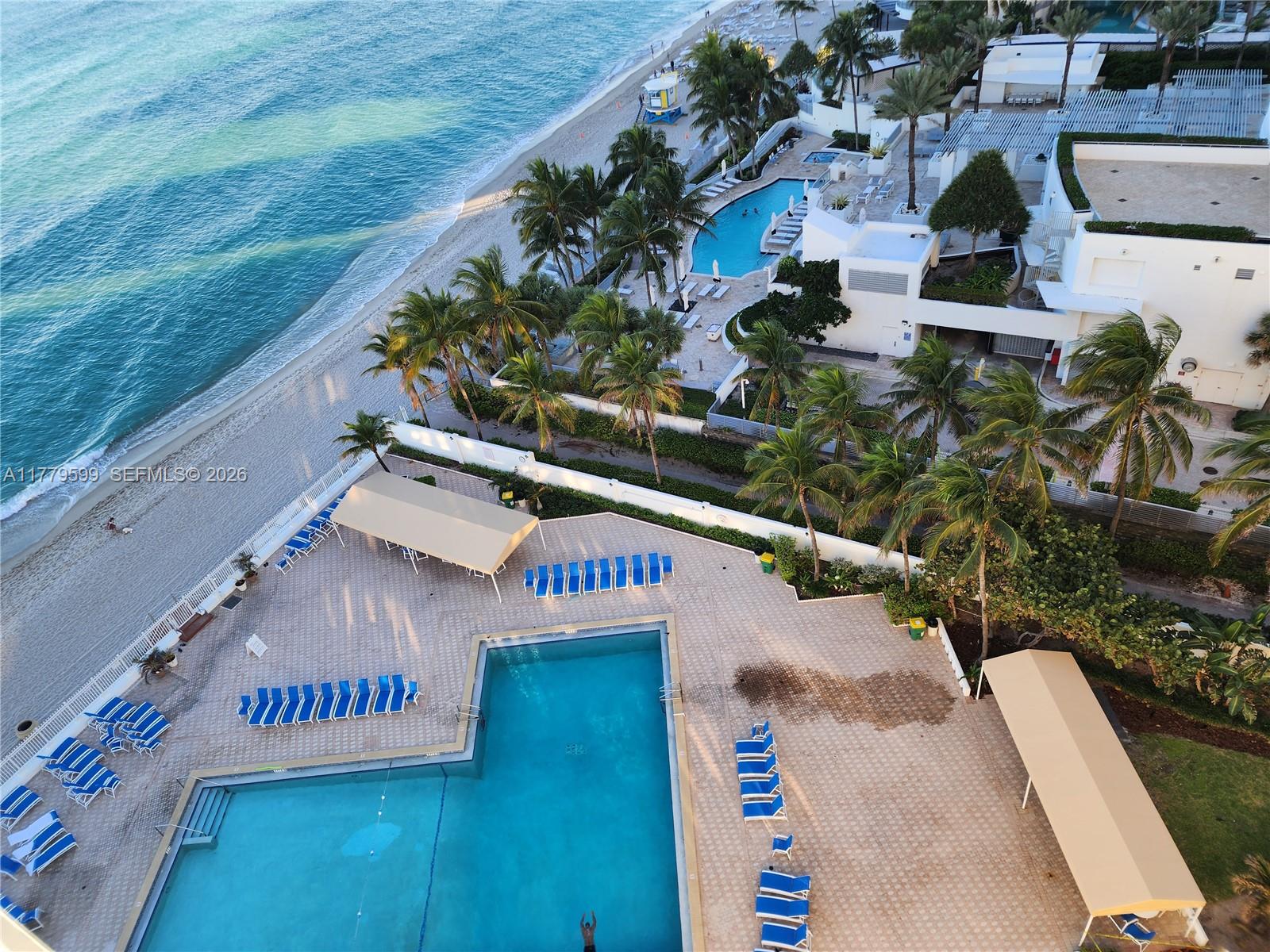 An aerial view shows a swimming pool area with lounge chairs next to a beach — 3505 S Ocean Dr # 1214, Hollywood FL 33019, HOLLYWOOD, FL