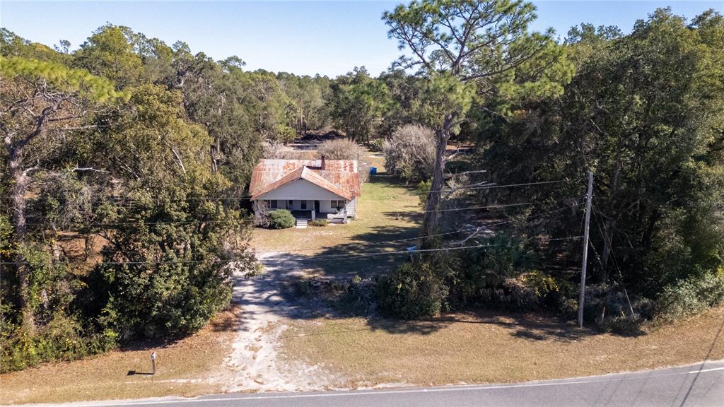 An aerial view shows a single-story house with a rusted metal roof amidst dense trees — 815 NE 145TH AVENUE ROAD, SILVER SPRINGS, FL
