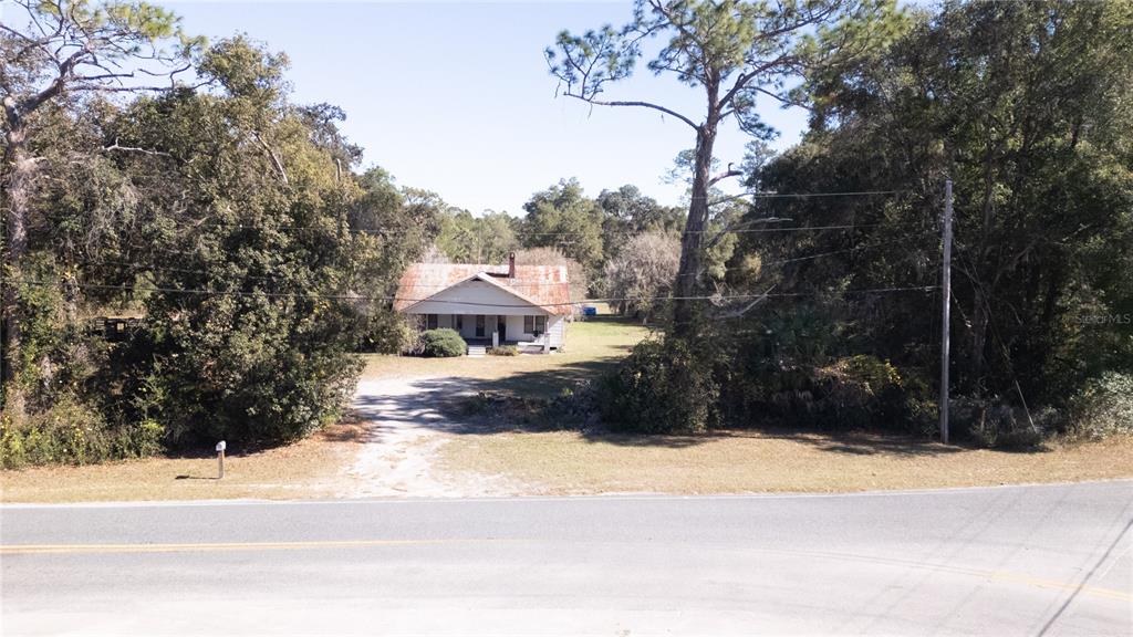 A single-story house with a rusted metal roof sits behind a dirt driveway and trees — 815 NE 145TH AVENUE ROAD, SILVER SPRINGS, FL