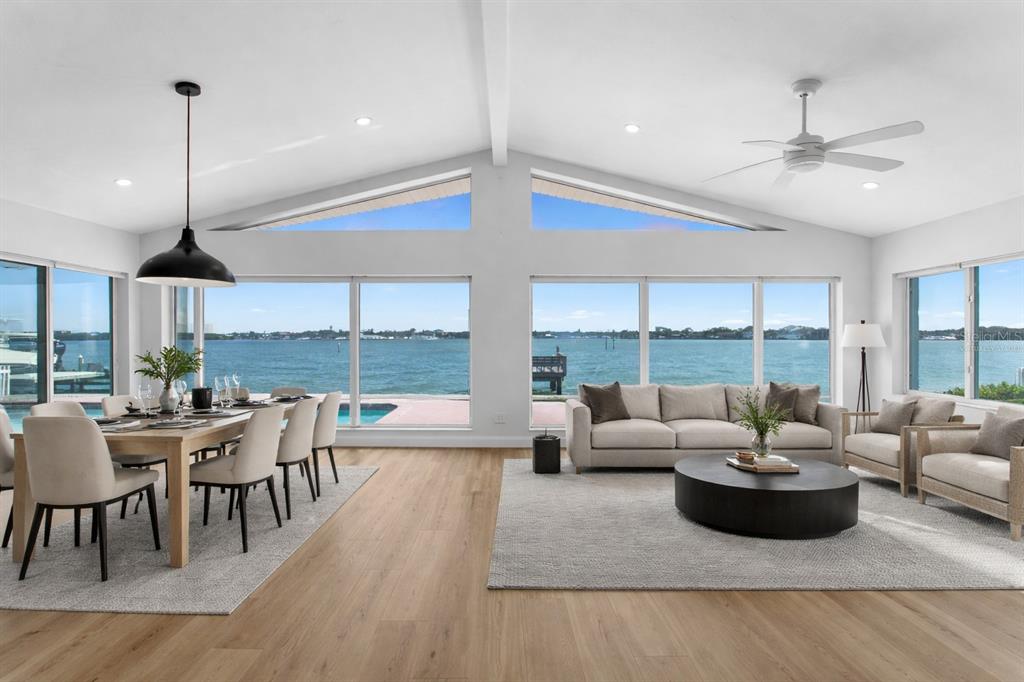 A bright, open-concept living and dining area features vaulted ceilings, large windows, and water views — 6984 S SHORE DRIVE S, ST PETERSBURG, FL