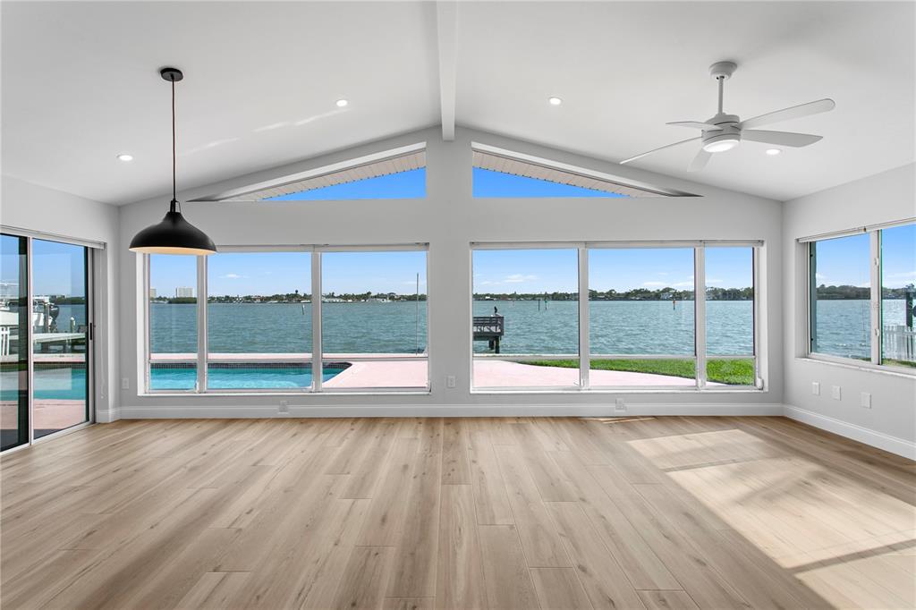 A bright living room with vaulted ceilings, light wood floors, and large windows overlooking water — 6984 S SHORE DRIVE S, ST PETERSBURG, FL