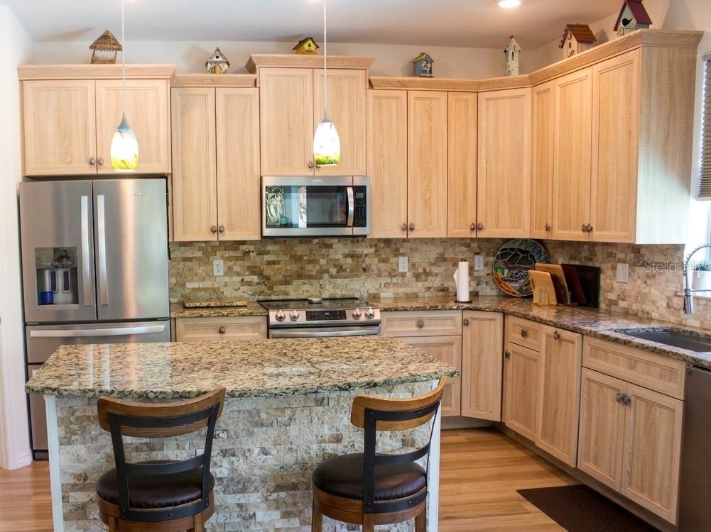 A kitchen features light wood cabinets, granite countertops, a stone backsplash, and a center island — 4 ULMACEA PLACE, PALM COAST, FL