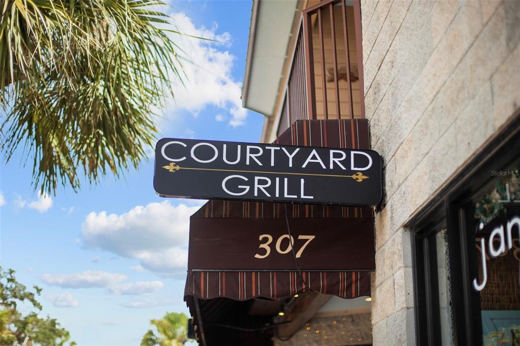 A sign for Courtyard Grill hangs above a striped awning on a stone building — 307 FLAGLER AVENUE UNIT 101, NEW SMYRNA BEACH, FL