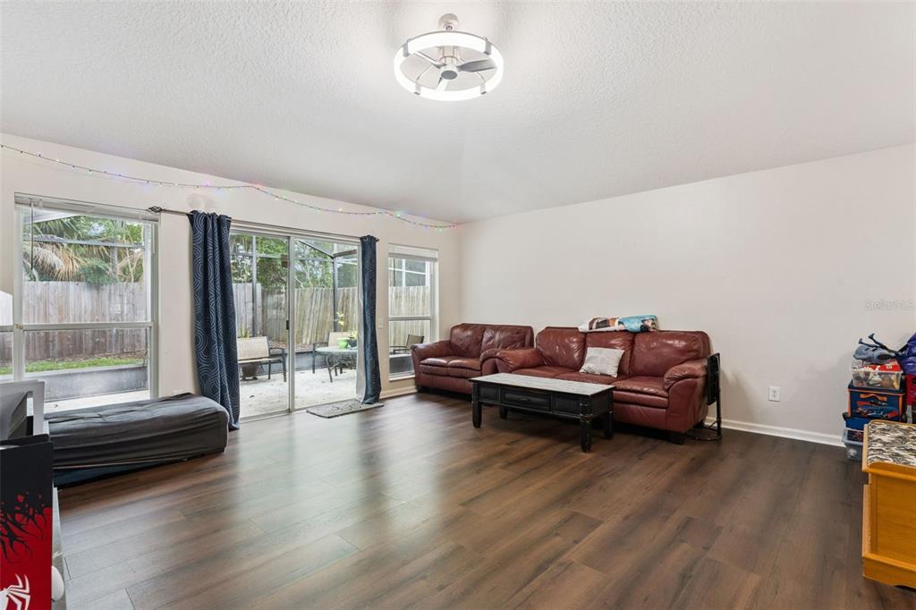 A living room with wood-look flooring, leather sofas, a ceiling fan, and sliding glass doors — 266 HANGING MOSS CIRCLE, LAKE MARY, FL
