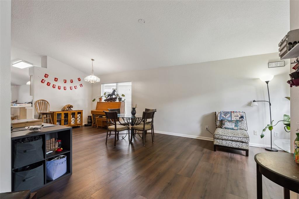 A dining area with wood-look flooring, a piano, and a patterned armchair in a living space — 266 HANGING MOSS CIRCLE, LAKE MARY, FL