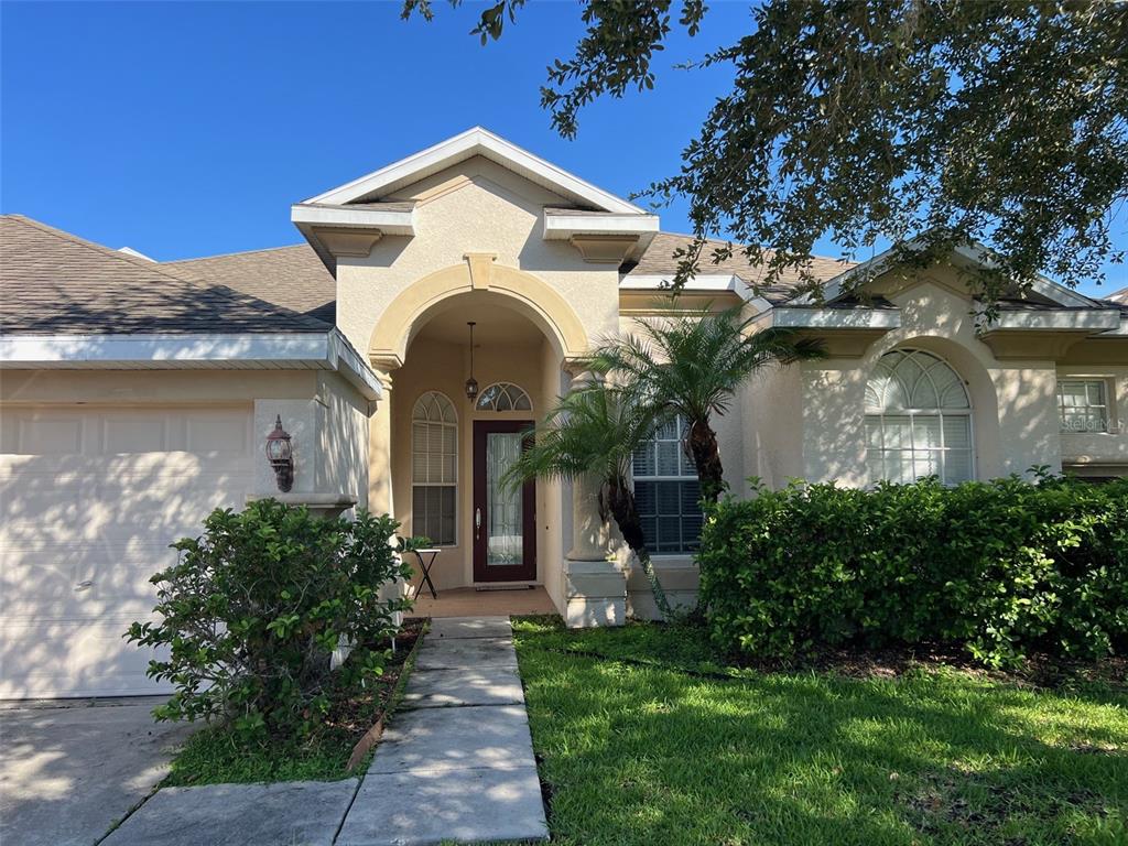 A single-story house exterior features a beige stucco facade, arched entryway, and a paved walkway — 4823 PORTMARNOCK WAY, WESLEY CHAPEL, FL