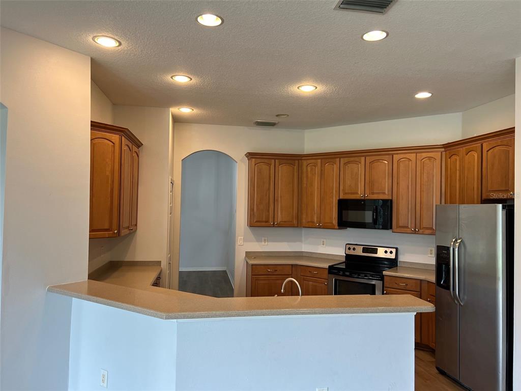 A kitchen features wood cabinets, stainless steel appliances, and a peninsula counter with beige countertops — 4823 PORTMARNOCK WAY, WESLEY CHAPEL, FL