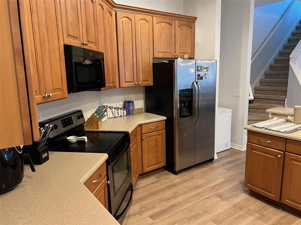A kitchen features wood cabinets, stainless steel appliances, and light-colored countertops with wood-look flooring — 4823 PORTMARNOCK WAY, WESLEY CHAPEL, FL