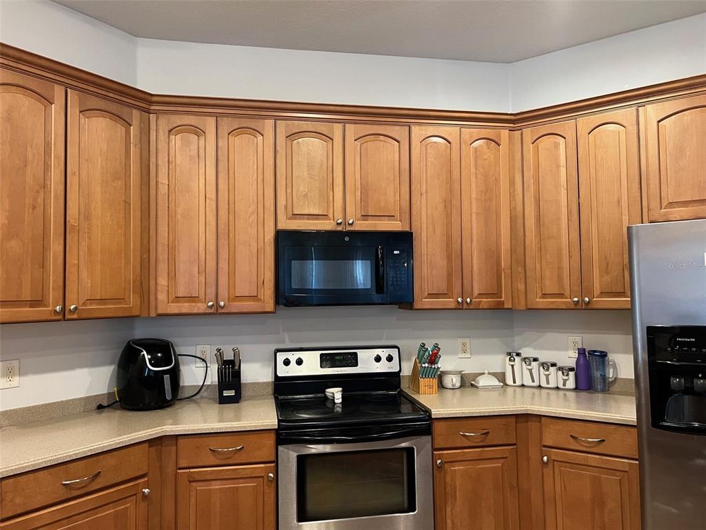 A kitchen features wood cabinets, stainless steel appliances, and light-colored countertops — 4823 PORTMARNOCK WAY, WESLEY CHAPEL, FL