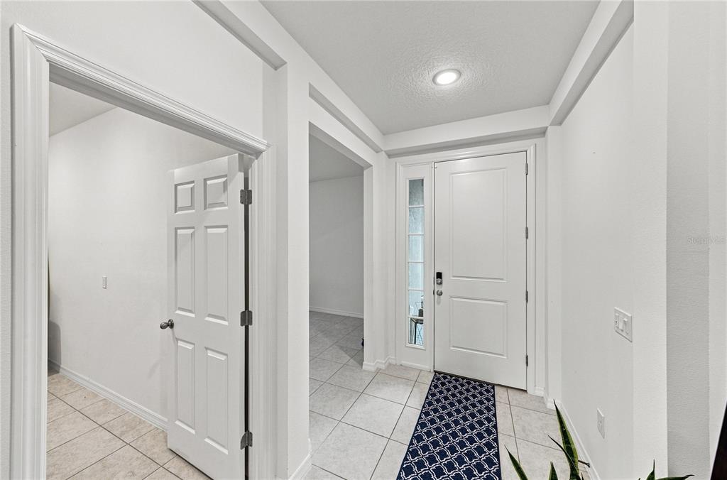 A covered entryway features a dark purple front door, gray stucco walls, and brick pavers — 2235 PIGEON PLUM DRIVE, HAINES CITY, FL