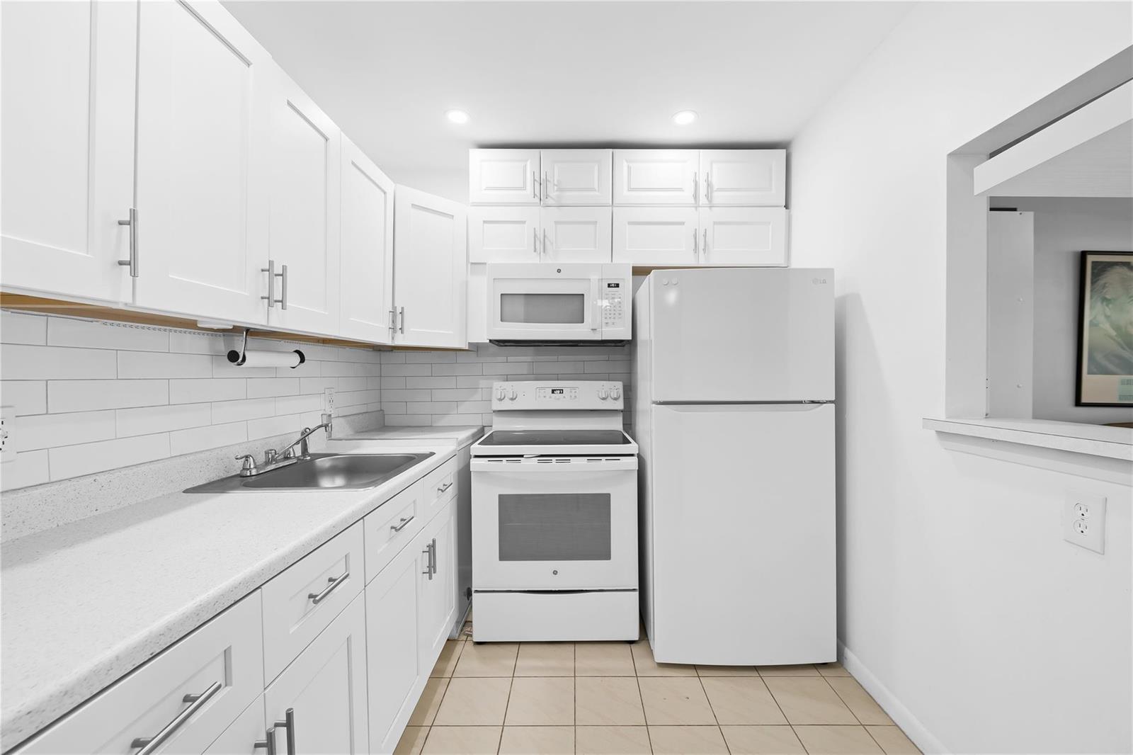 A galley kitchen features white cabinets, white appliances, a tiled backsplash, and light-colored floor tiles — 39 Prescott B # 39, Deerfield Beach FL 33442, DEERFIELD BEACH, FL