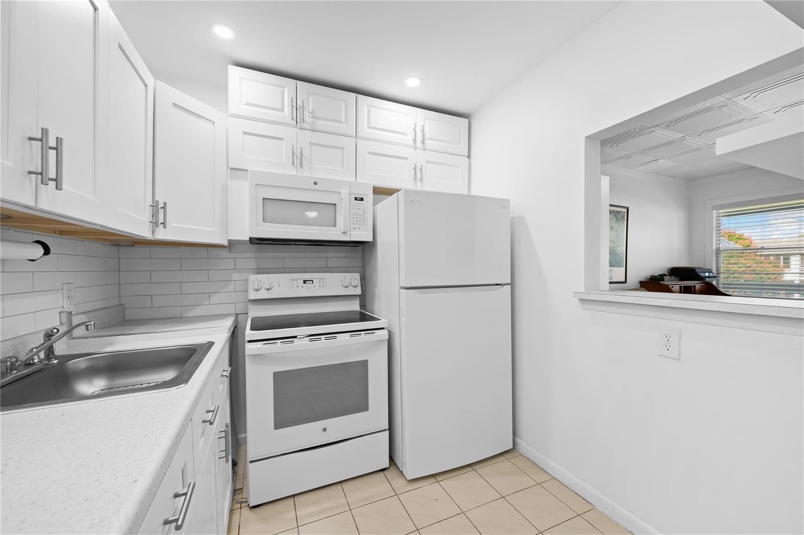 A kitchen features white cabinets, white appliances, a subway tile backsplash, and a pass-through window — 39 Prescott B # 39, Deerfield Beach FL 33442, DEERFIELD BEACH, FL