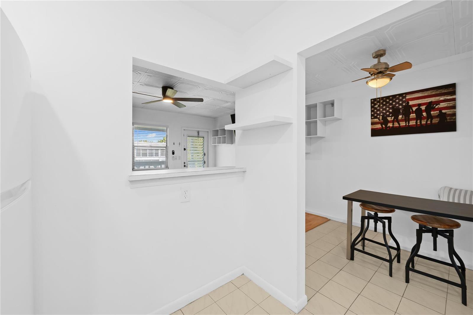 A kitchen pass-through window overlooks a dining area with a table, stools, and ceiling fan — 39 Prescott B # 39, Deerfield Beach FL 33442, DEERFIELD BEACH, FL