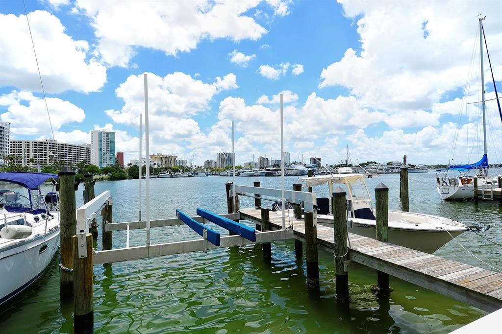 A boat lift and wooden dock sit in a marina with boats and city buildings — 650 GOLDEN GATE POINT UNIT 602, SARASOTA, FL