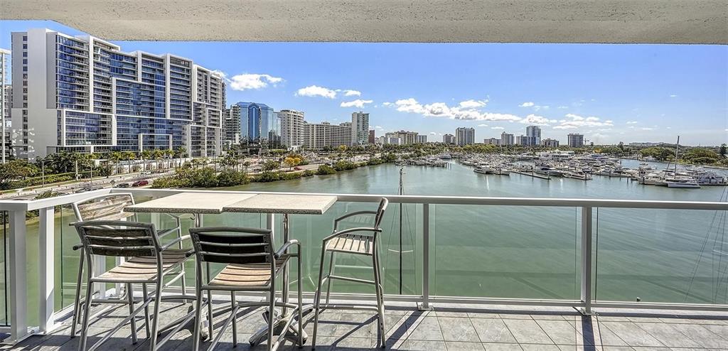 A balcony with a table and chairs overlooks a marina and city skyline — 650 GOLDEN GATE POINT UNIT 602, SARASOTA, FL