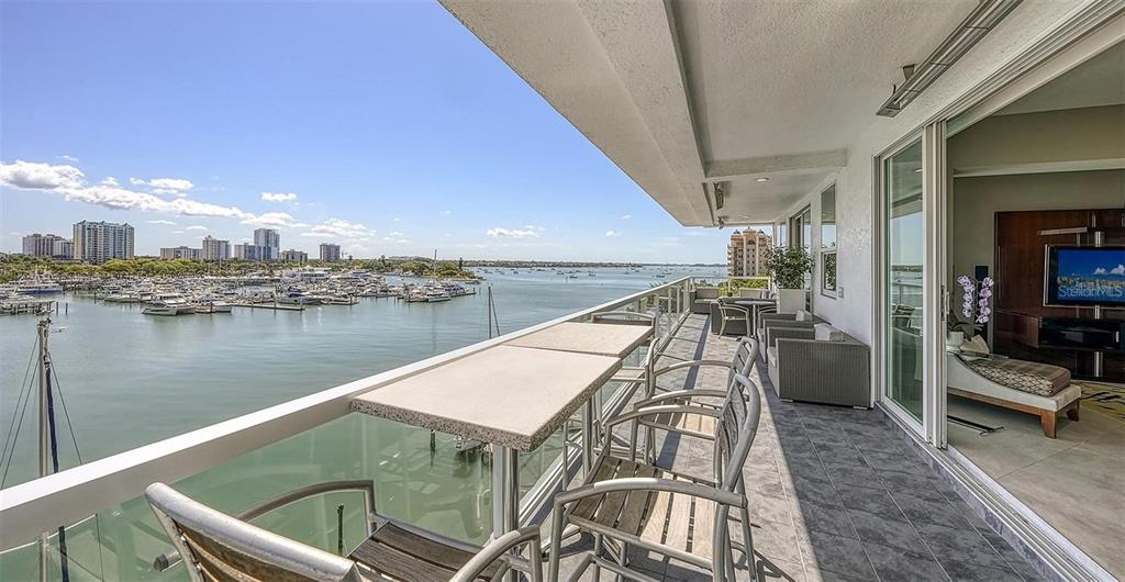 A balcony with outdoor seating overlooks a marina and city skyline under a blue sky — 650 GOLDEN GATE POINT UNIT 602, SARASOTA, FL
