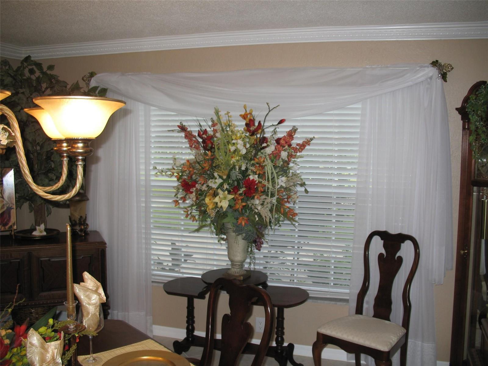 A dining room features a window with white curtains, a floral centerpiece, and wooden chairs — 555 SW 87th Place, Ocala FL 34476, OCALA, FL