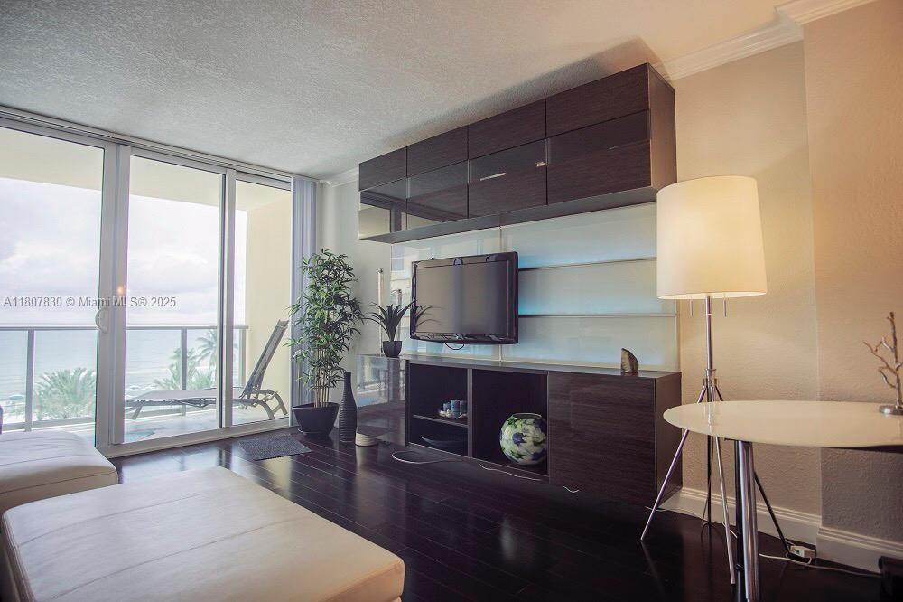A living room features dark wood floors, a wall-mounted television unit, and a balcony view — 2501 S Ocean Dr # 520, Hollywood FL 33019, HOLLYWOOD, FL