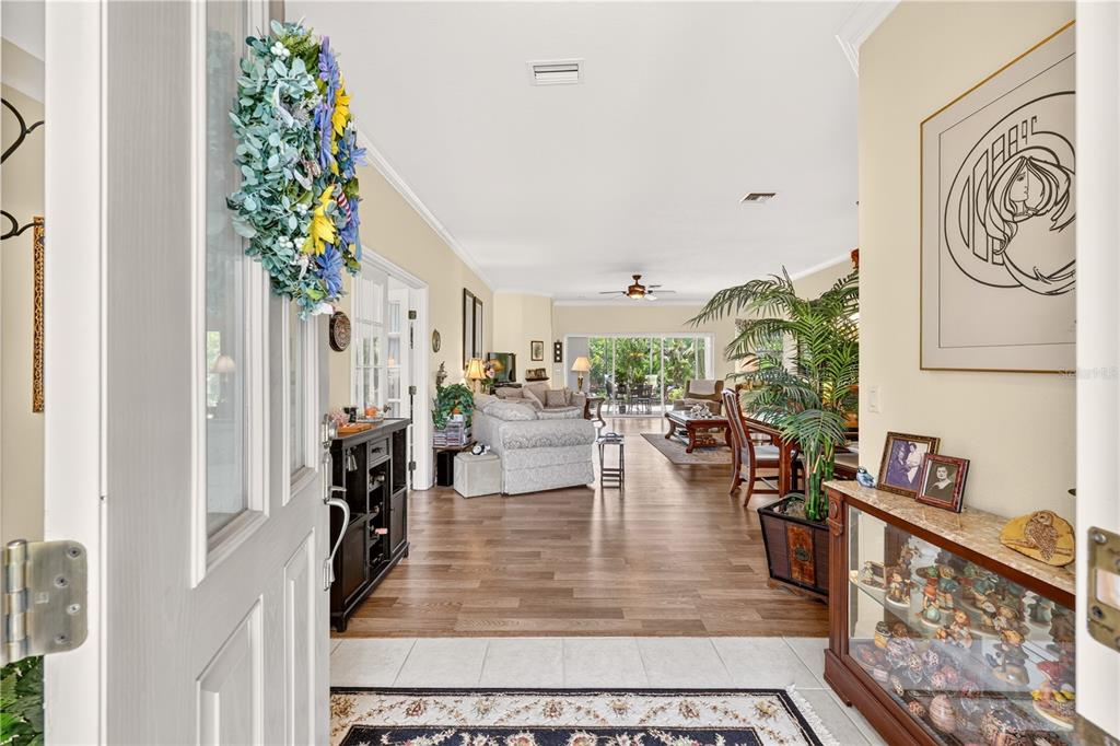 A view from an open front door into a living room with wood-look flooring — 10055 SW 90TH LOOP, OCALA, FL
