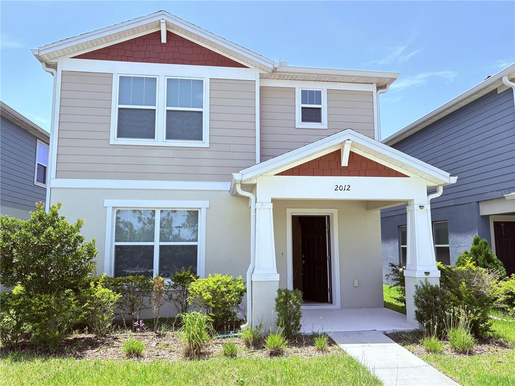 A two-story house with beige siding, a front porch, and a small patch of landscaping — 2012 CROSS PRAIRIE PARKWAY, KISSIMMEE, FL