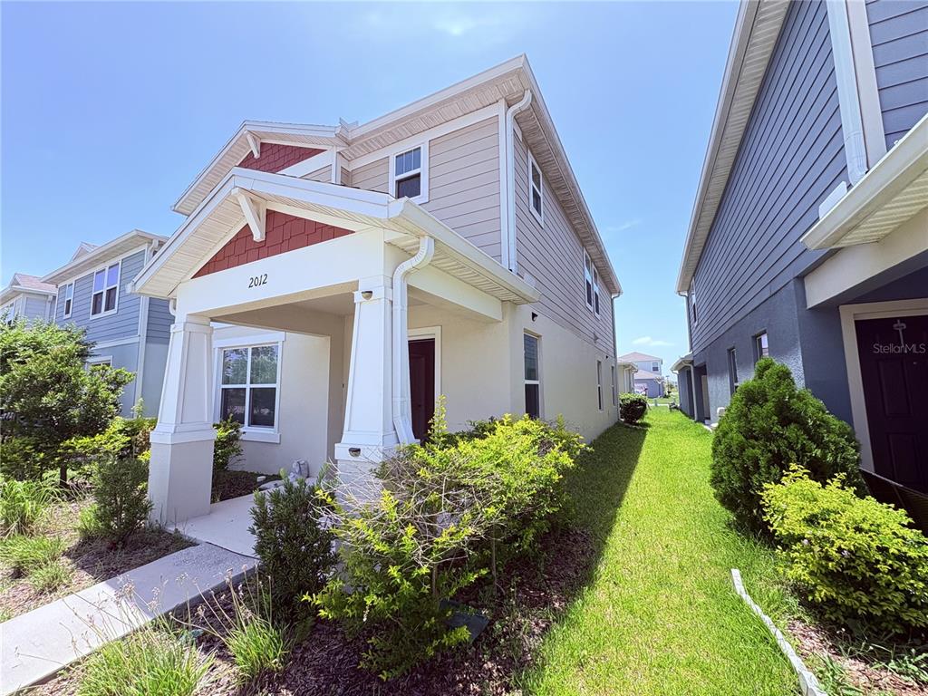 A two-story house with beige siding, a red shingled gable, and a covered front porch — 2012 CROSS PRAIRIE PARKWAY, KISSIMMEE, FL