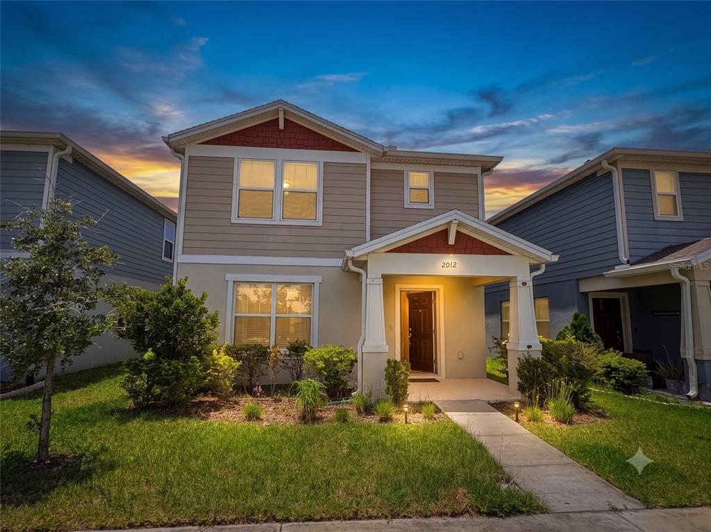 A two-story house with tan siding, a front porch, and a small landscaped yard — 2012 CROSS PRAIRIE PARKWAY, KISSIMMEE, FL