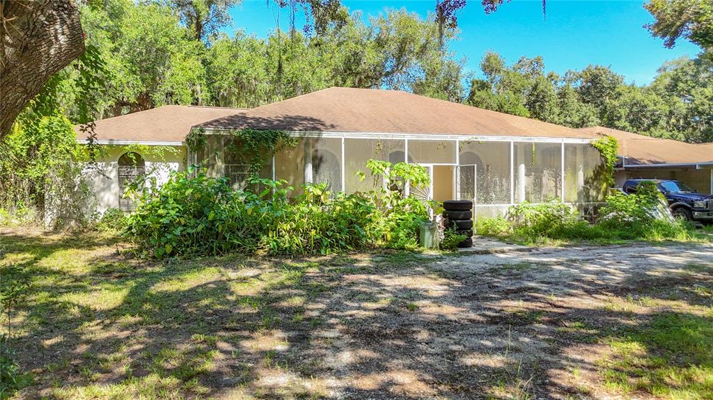 A single-story house with a large screened-in porch and overgrown landscaping in the yard — 7350 PALOMINO TRAIL, SARASOTA, FL