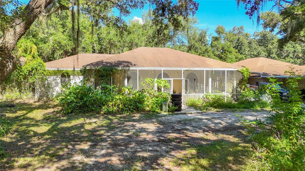 A single-story house with a screened-in porch is surrounded by overgrown vegetation and trees — 7350 PALOMINO TRAIL, SARASOTA, FL